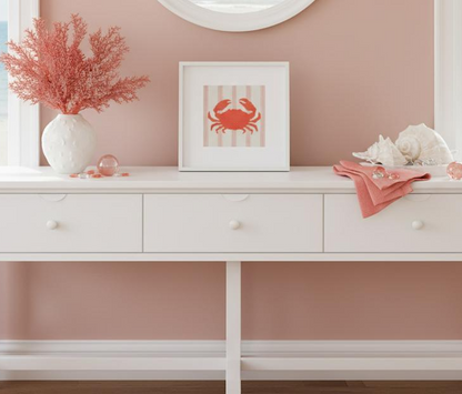 White dresser with decorative items including a vase with pink flowers, a framed picture of a crab, and a pink towel against a pink wall.