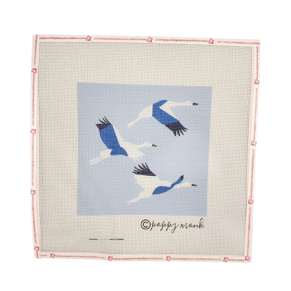 A square needlepoint canvas featuring three flying blue and white cranes on a light blue background, surrounded by a beige mesh border with a pink stitched edge and the brand name &