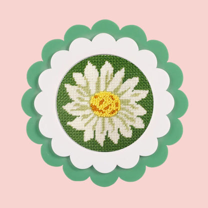 A daisy needlepoint round with decorative stitches shown in a green scalloped frame