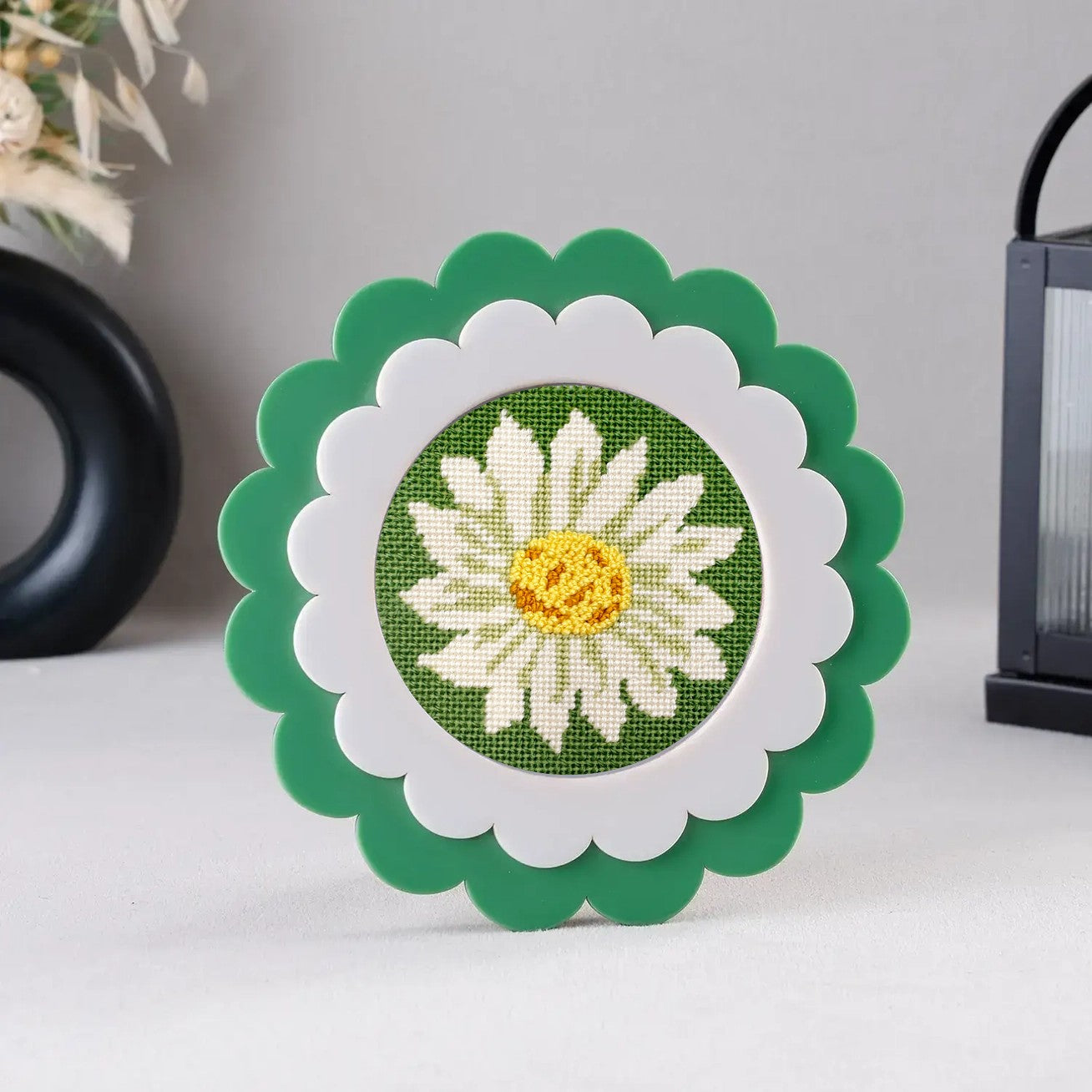 A daisy needlepoint round with decorative stitches shown in a green scalloped frame