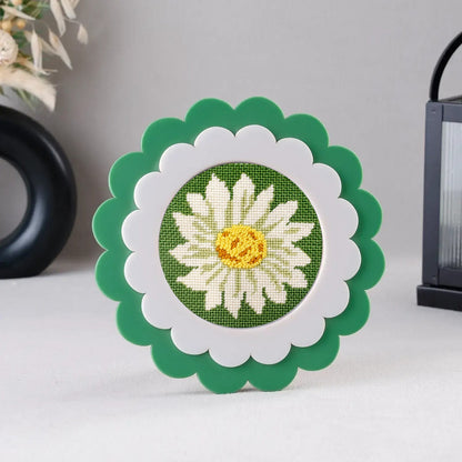 A daisy needlepoint round with decorative stitches shown in a green scalloped frame