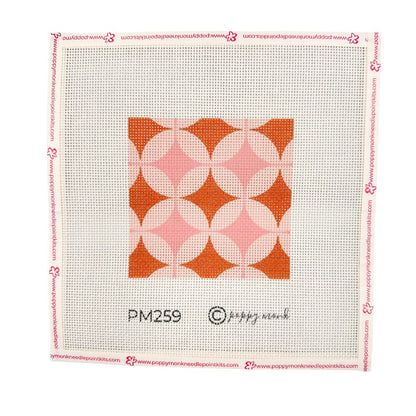 A geometric needlepoint design in orange and pinks shown in a white frame