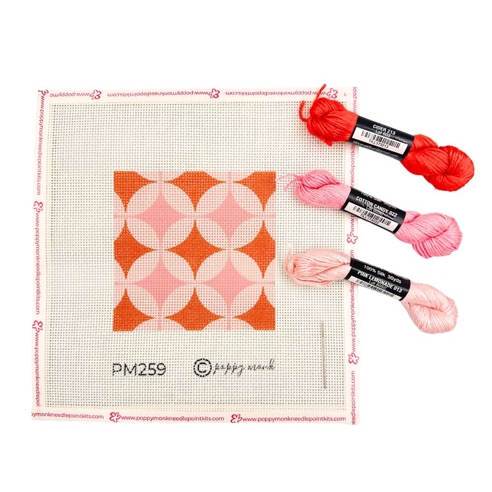 A geometric needlepoint design in orange and pinks shown with three skeins of thread