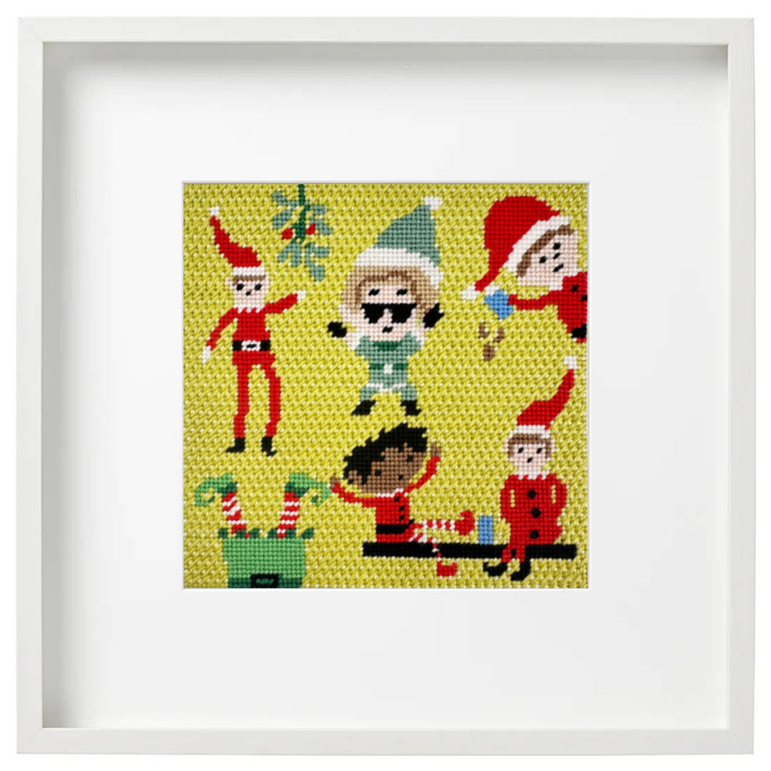 A framed needlepoint artwork featuring multiple Christmas elf characters on a yellow background, presented in a white square frame with a wide white mat.