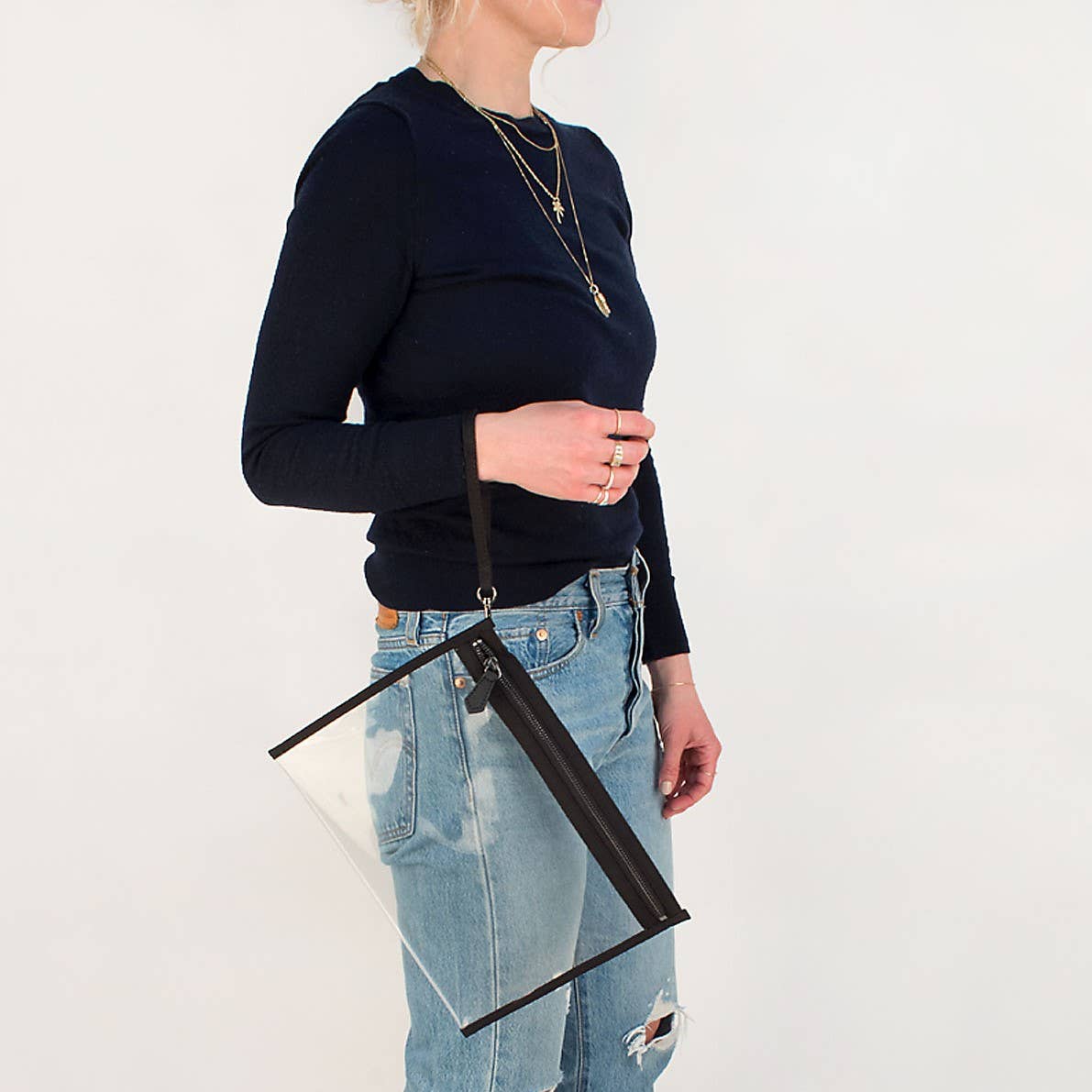 Person wearing a navy sweater and blue jeans holding a clear handbag with a black strap.