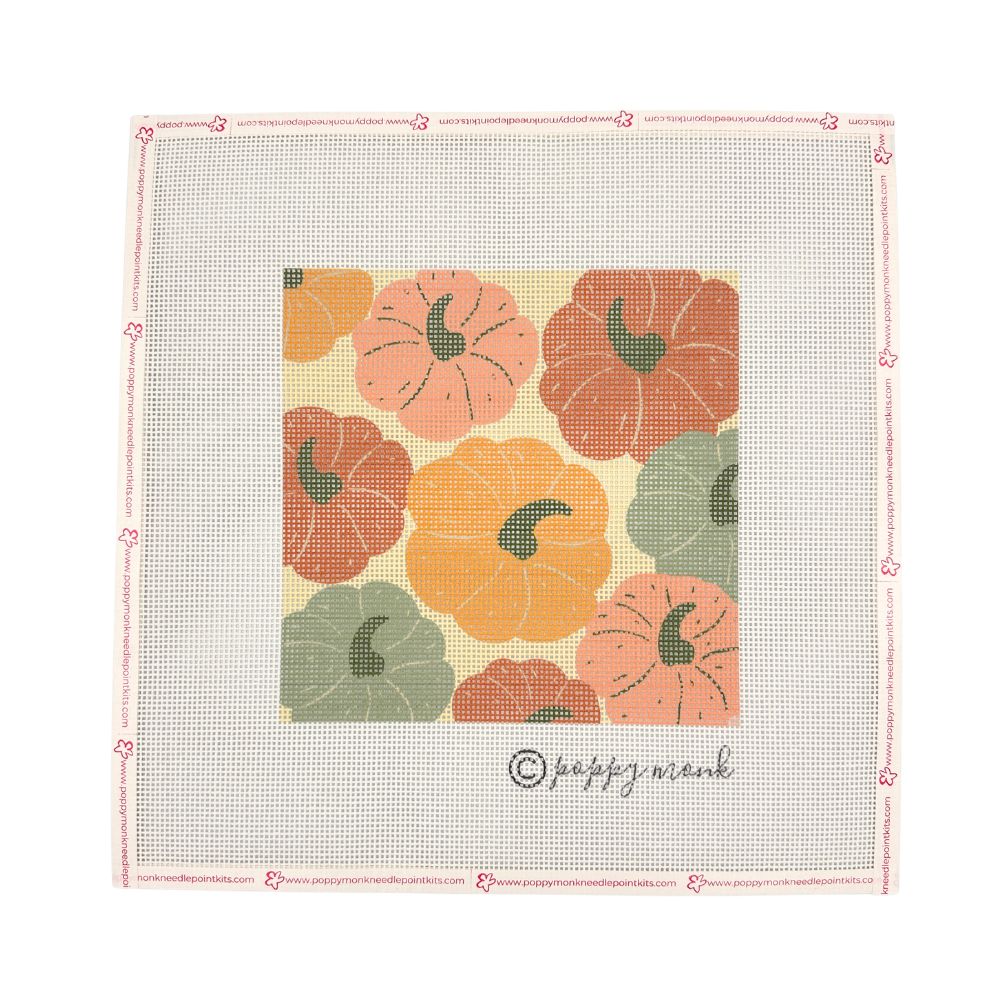 A square needlepoint canvas featuring a central design of stylized pumpkins in orange, peach, and green on a cream background, surrounded by a light pink stitched border with small floral accents and the brand name &