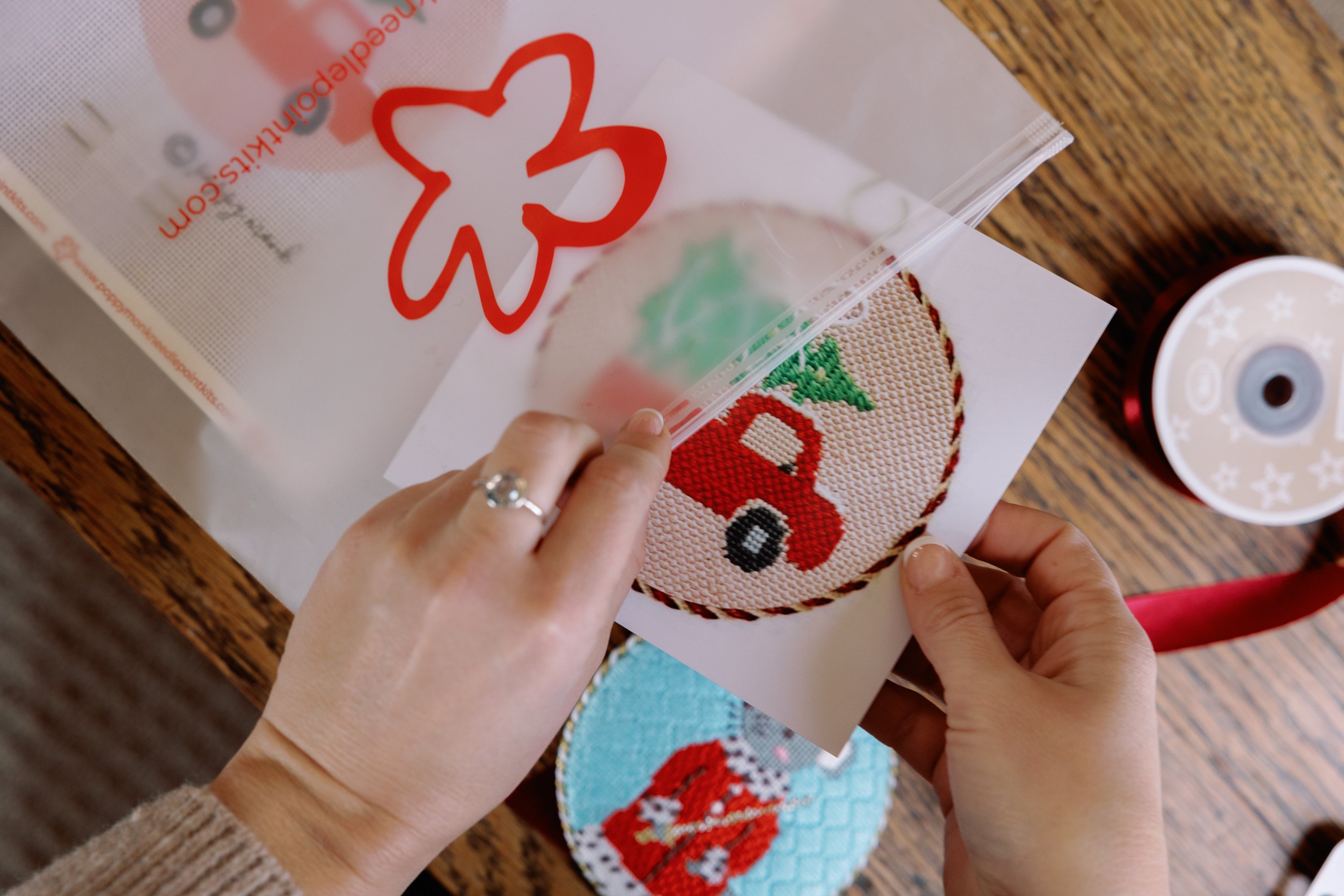 Person holding a piece of paper with a red car design over a fabric patch on a wooden table.