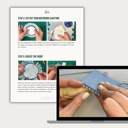 A printed sewing or matboard-cutting instruction sheet shown beside a laptop screen displaying a close-up of hands working on a blue fabric mat. The sheet includes step-by-step text and photos, and the laptop screen shows the corresponding tutorial content.
