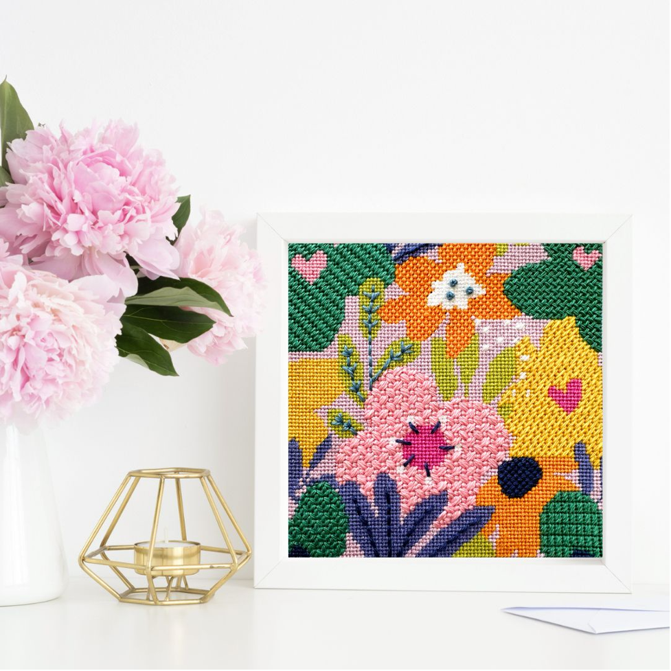 Floral cross-stitch pattern on a white background with pink flowers and a gold candle holder.
