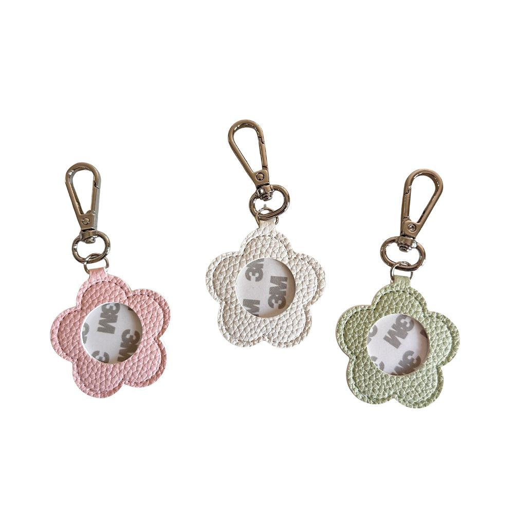 Three flower-shaped keychains in  pink, white, and green with a metal clasp on a white background