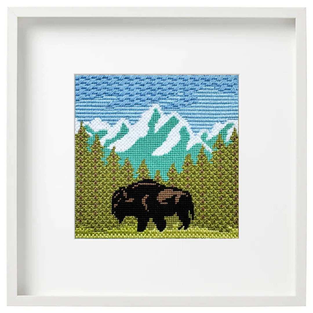 Framed cross-stitched artwork of a mountain landscape with a bison.