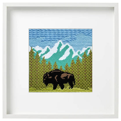 Framed cross-stitched artwork of a mountain landscape with a bison.