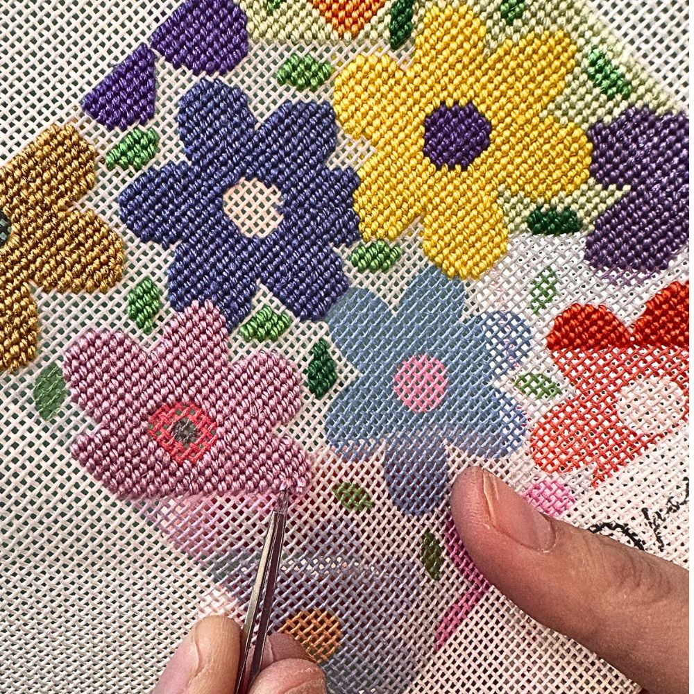 Cross-stitched flowers on fabric with a hand holding a needle.