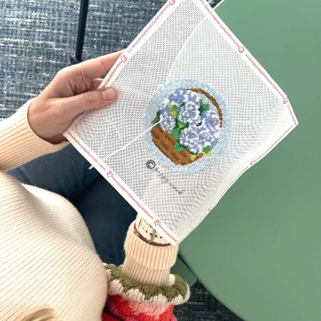 Hand holding a needlepoint piece with a floral design on a textured surface