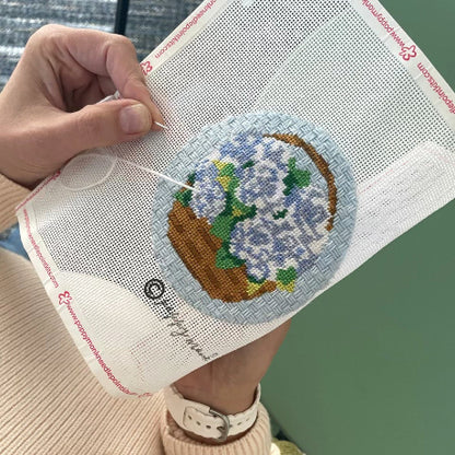 Hand holding a needlepoint fabric with a floral design on a green background