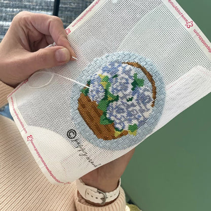 Hand holding a needlepoint fabric with a floral design on a green background