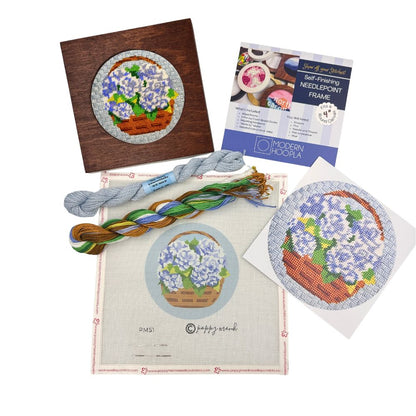 Needlepoint kit with completed sample, thread, and instructions on a white background