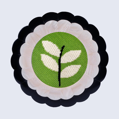 A green and white round needlepoint design in a scalloped frame