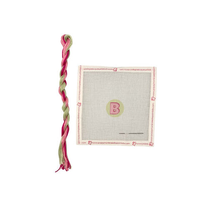 Pink and green braided toy with a cardboard tag featuring a letter &