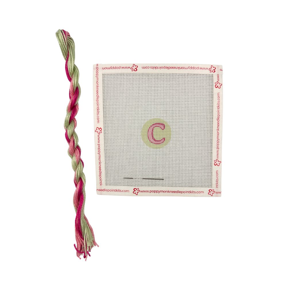 Cross-stitch kit with a pre-printed pattern and braided pink and green thread on a white background.