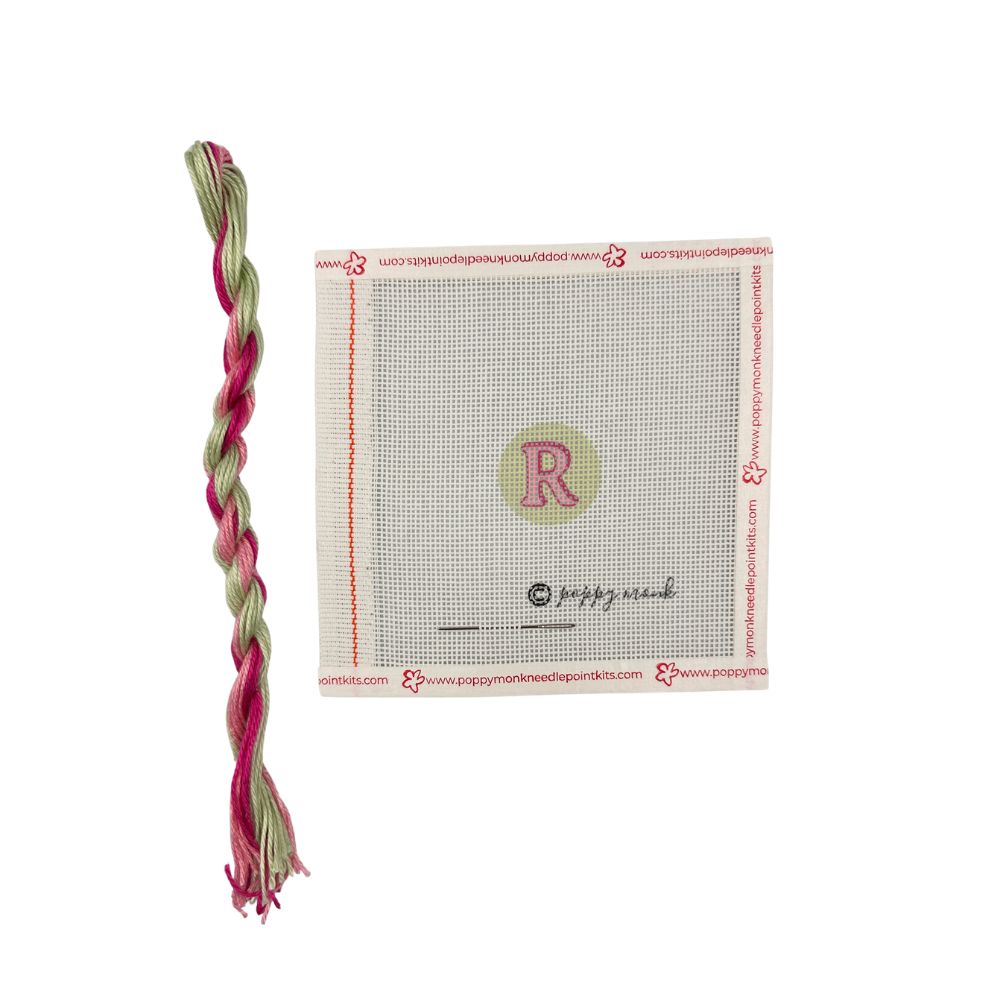 Braided pink and green yarn with a cross-stitching mat featuring a letter &