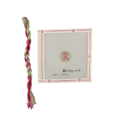 Braided pink and green yarn with a cross-stitching mat featuring a letter &