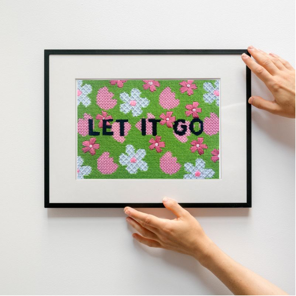 Framed cross-stitched artwork with floral patterns and 'LET IT GO' text on a white background