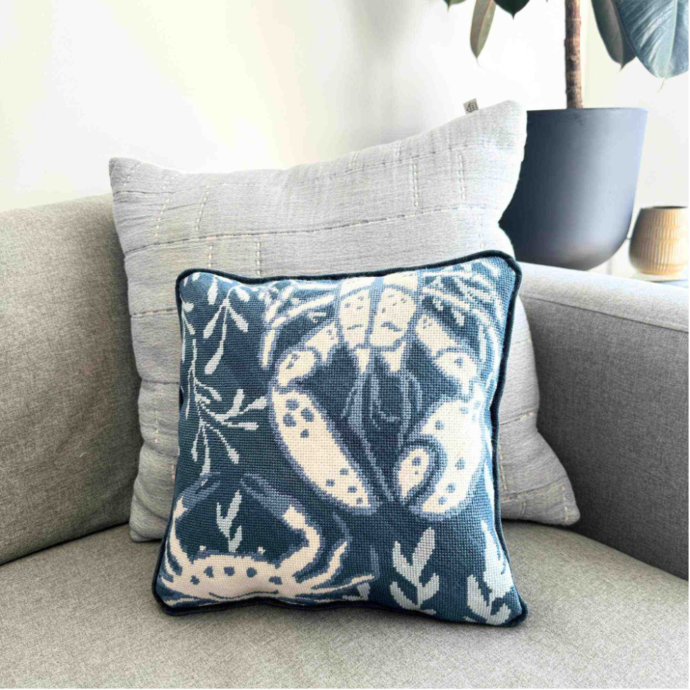 Decorative needlepoint pillow with blue and white pattern on a gray sofa