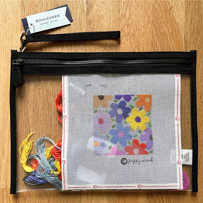 Embroidery kit with colorful flowers on a clear plastic case, on a wooden surface.