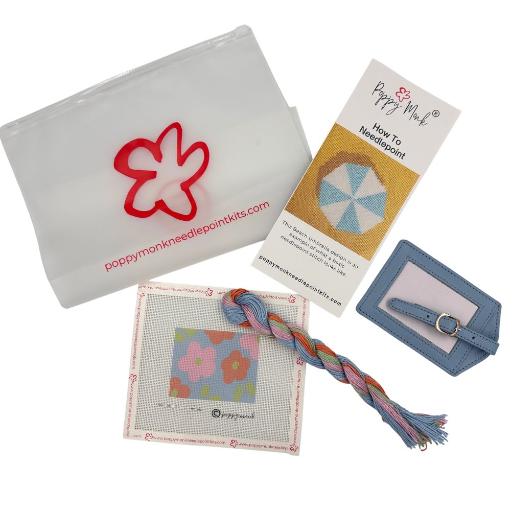Poppy Monk Needlepoint Kits starter kit containing a white drawstring pouch with a red flower logo, an instruction card, a blue leather tag, and a finished floral needlepoint canvas with a braided multicolor thread.