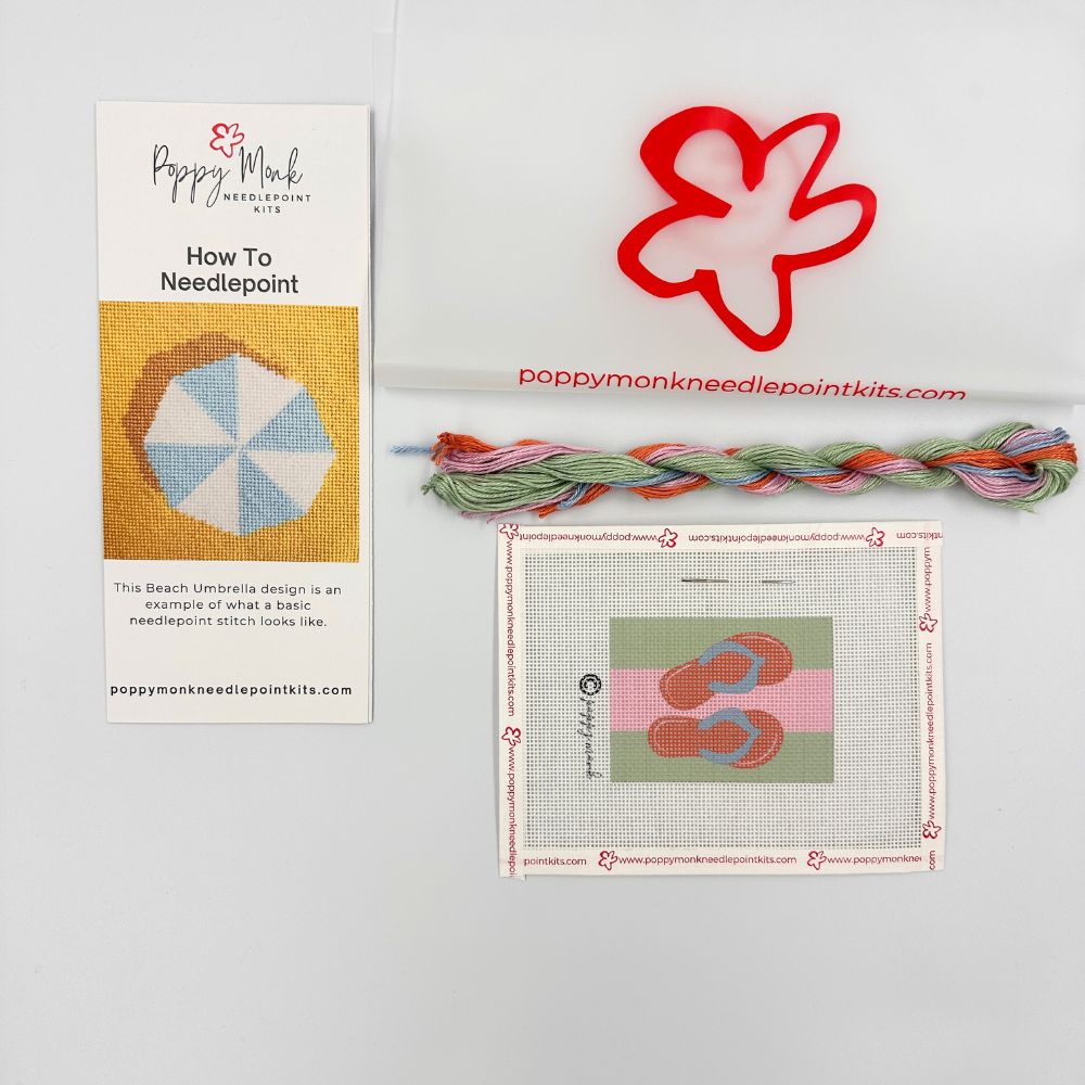 Poppy Monk needlepoint kit with instructions, thread, and a red flower-shaped tool on a white background.