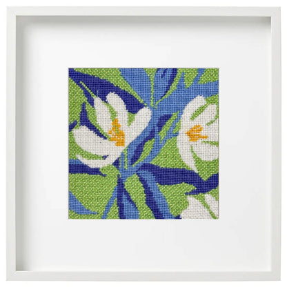 Framed needlepoint artwork of white magnolia flowers with blue leaves on a green background