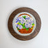 Round wooden framed cross-stitched piece with flowers on a white background
