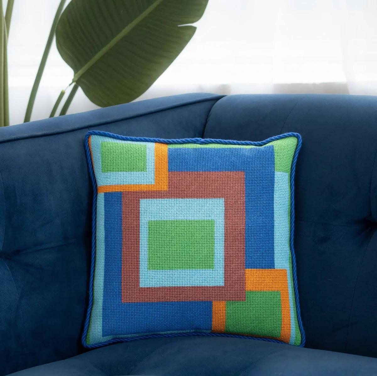 Abstract needlepoint pillow shown on a sofa
