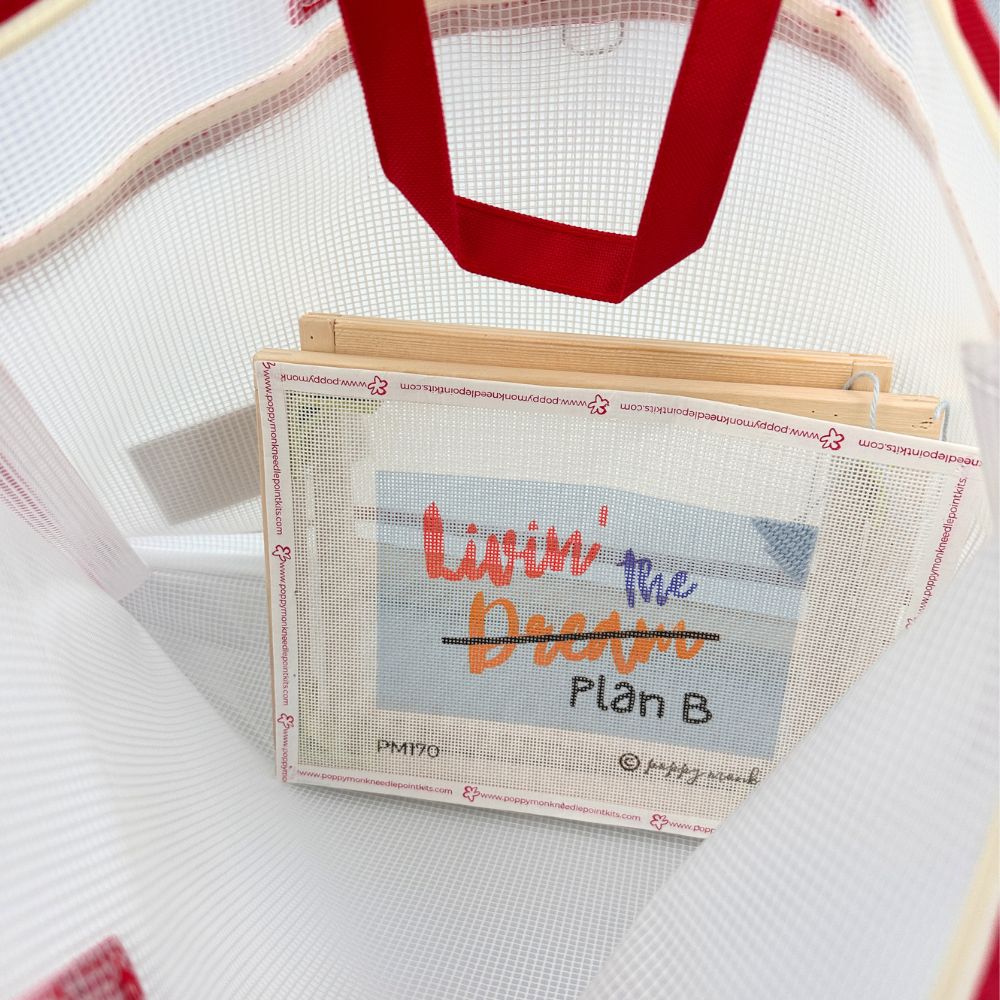 A close-up of a white mesh tote bag with red handles, holding a small printed card that reads &