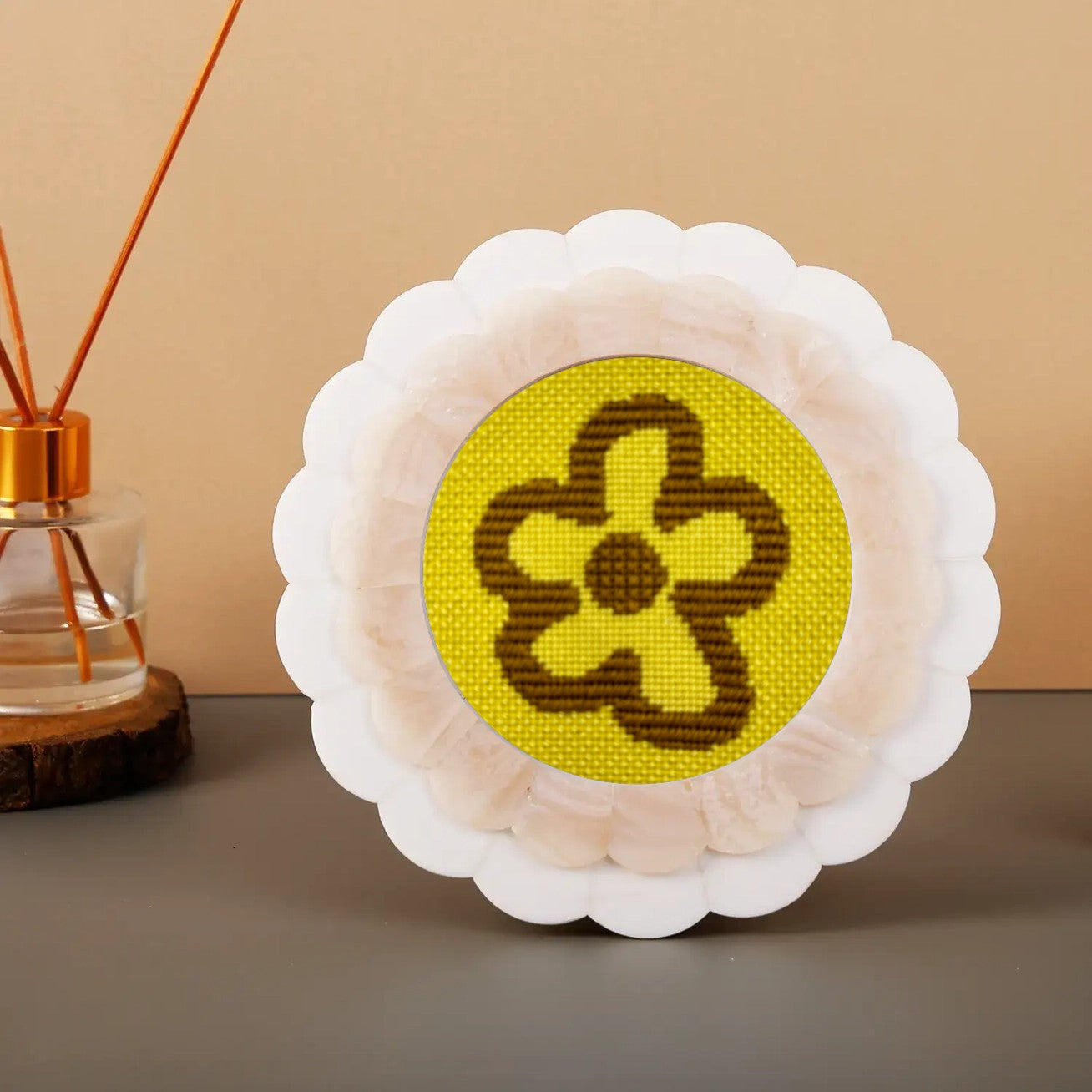 A modern floral motif needlepoint design in neon yellow and khaki shown in a round scalloped frame