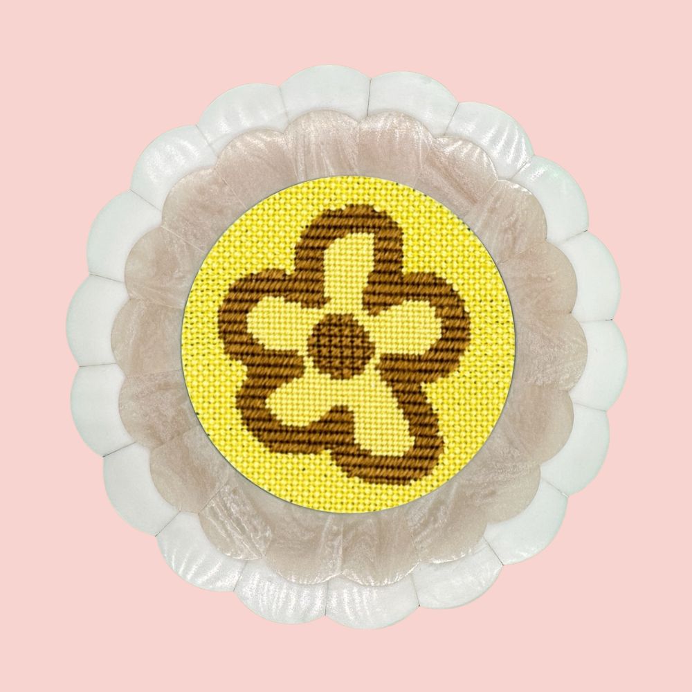 A modern floral motif needlepoint design in neon yellow and khaki shown in a round scalloped frame