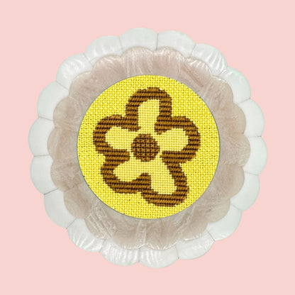 A modern floral motif needlepoint design in neon yellow and khaki shown in a round scalloped frame