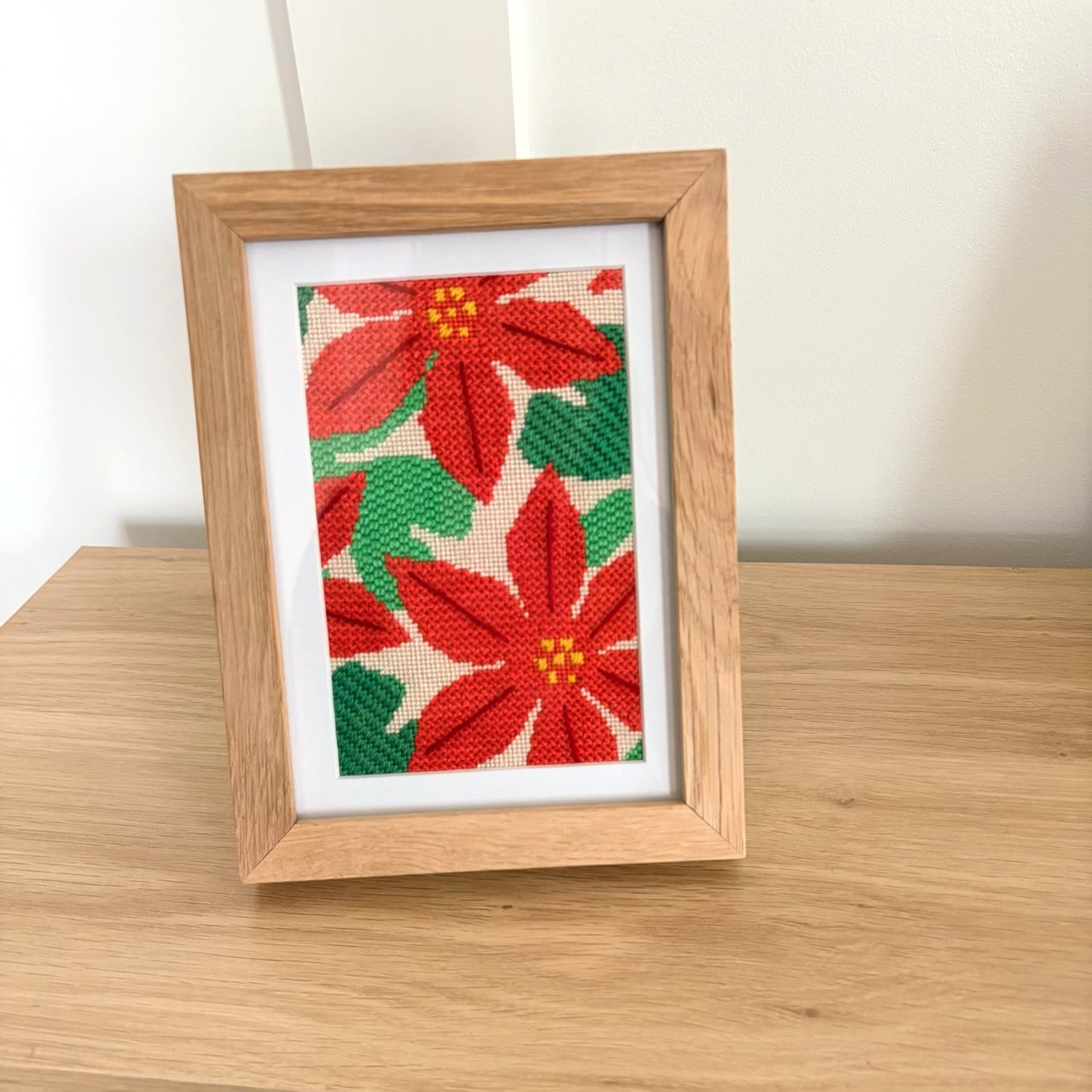 Framed needlepoint poinsettia design on a wooden surface