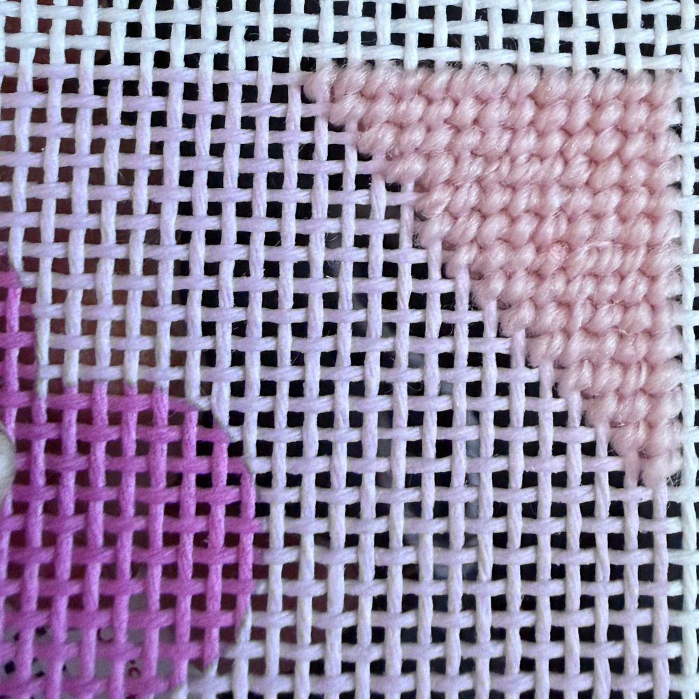 Needlepoint stitches with pink and purple patterns on a white grid background