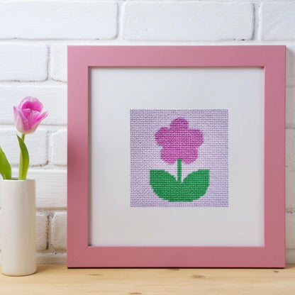 Framed needlepoint pink flower on a white background with a pink frame.