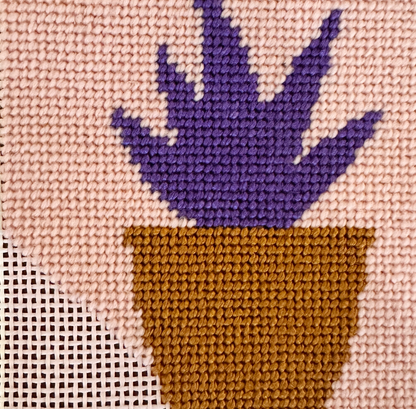 Needlepoint purple plant in a brown pot on beige fabric