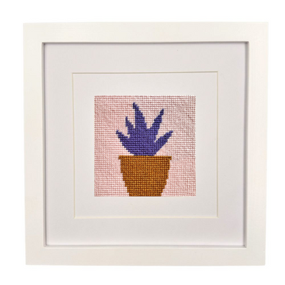 Framed needlepoint artwork of a potted plant on a white background
