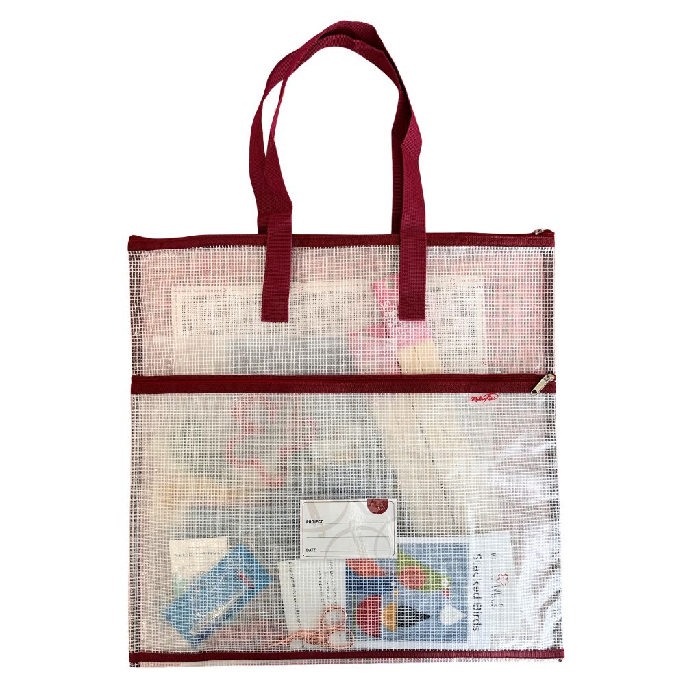 Mesh tote bag with red handles filled with needlepoint items on a white background