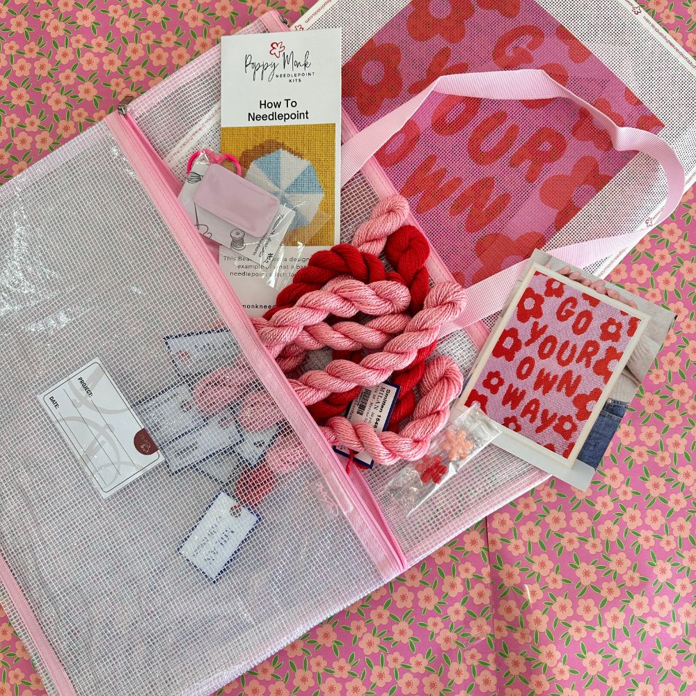 Needlepoint kit with bag, fabric, thread, and instructions on a floral background