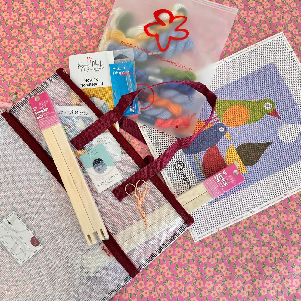 Collection of needlework supplies including thread, needles, and a pattern book on a floral background.