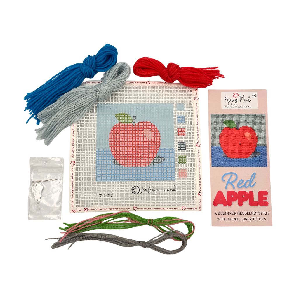 Needlepoint kit with red apple design, thread, and packaging on a white background