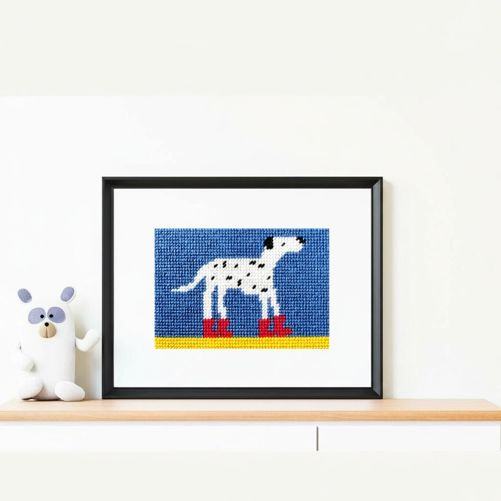 Framed needlepoint of a Dalmatian dog on a white wall with a toy to the left.