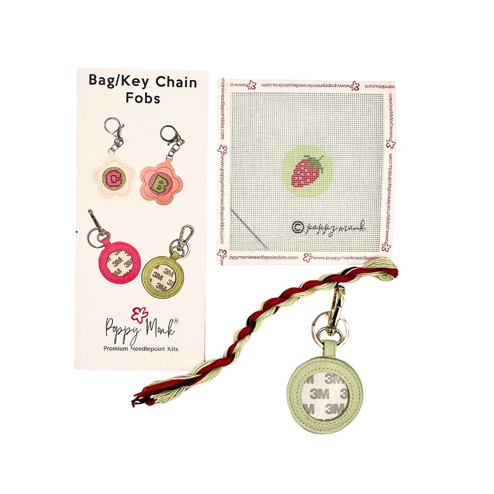 A needlepoint kit with a small round strawberries design with fob hardware.