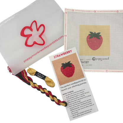 Needlepoint kit with strawberry design, yarn, and instructions on a white background